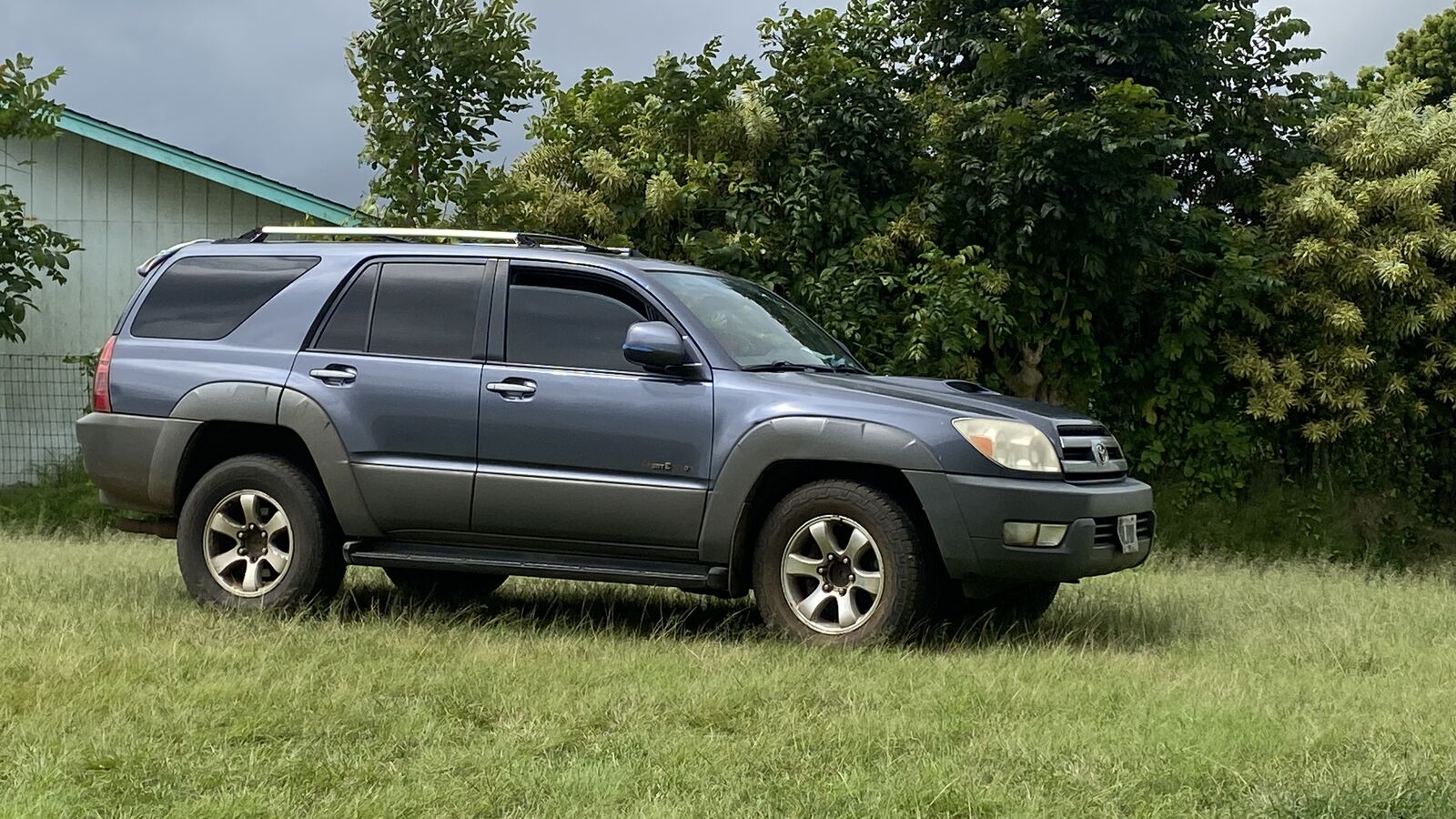 A blue-grey Toyota 4Runner parked on grass beside a treeline